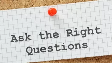 Note on corkboard reading 'Ask the Right Questions' with a pushpin.