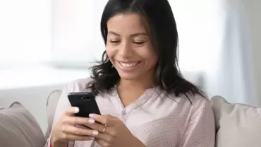 Persoon zit op de bank en kijkt naar een smartphone met een glimlach