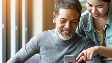 Twee mensen glimlachen terwijl ze samen naar een telefoon kijken.