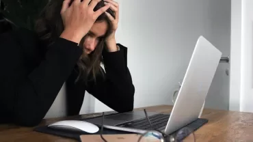 Persoon met handen in het haar voor een laptop op een bureau.