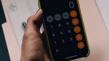 Telefoon met rekenmachine-app naast documenten op een bureau.