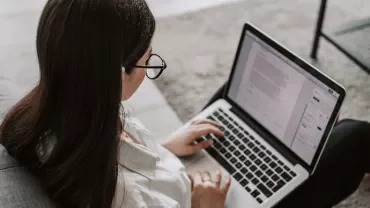 Persoon werkt op een laptop zittend op een bank.