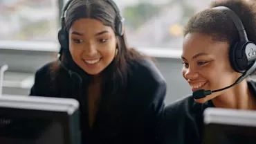 Twee mensen met hoofdtelefoons werken samen achter computers.