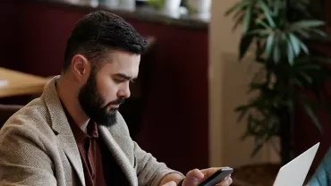 Persoon zit in café met laptop en telefoon.