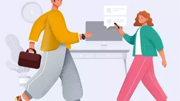 Two people talking near a desk with a computer.