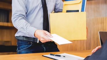 Een werknemer, gekleed in overhemd en das, draagt een doos met documenten en overhandigt een ontslagbrief aan zijn baas.