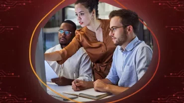 Drie mensen werken samen in een kantoor aan een project met documenten en laptops.