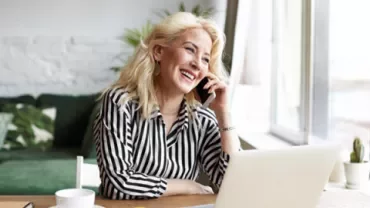 Person smiling while talking on phone and working on a laptop.