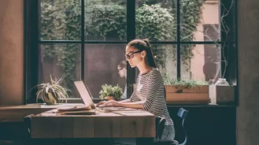 A person working on a laptop in a sunlight-filled café.