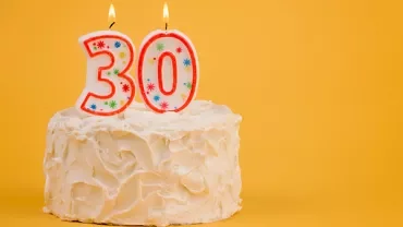 White cake with burning 30-shaped candles on yellow background.