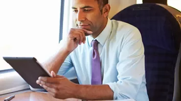 Man leest op een tablet in een trein, documenten en pen op tafel.