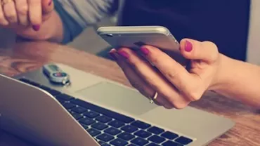 Person using a smartphone next to a laptop with a USB drive.