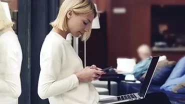 Person sitting with a laptop and using a phone.