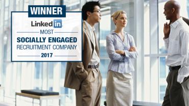 Three people conversing in front of a sign showing a LinkedIn award.
