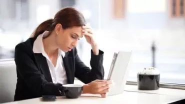 Persoon in een café kijkt vermoeid naar een tablet.