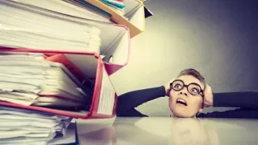 Person wearing glasses looking at a large stack of papers.