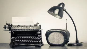 Typemachine met een retro radio en bureaulamp op een houten tafel.
