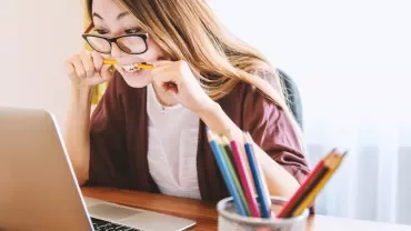 Person biting a pencil while looking at a laptop.
