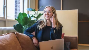 Vrouw glimlacht tijdens een telefoongesprek, met laptop op schoot.