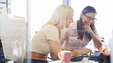 Twee personen glimlachen en kijken naar een laptop op kantoor.