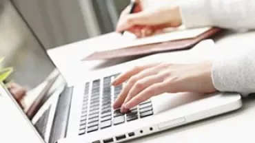 Een persoon typt op een laptop en maakt aantekeningen.