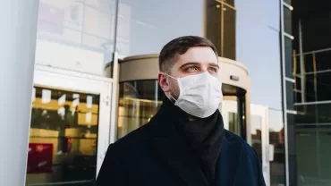 Person wearing a mask outside a building with glass doors
