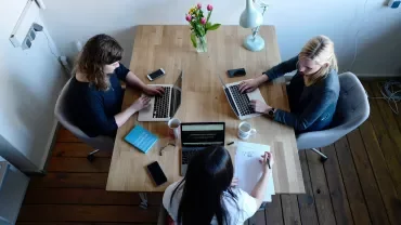 Three people working at a table with laptops and coffee.
