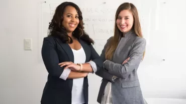 Two people in business attire standing in front of a whiteboard.