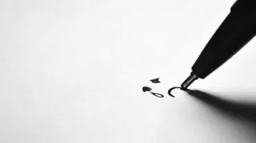 A pen drawing a simple face on white paper.