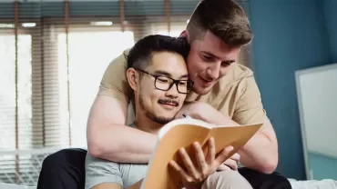 Two people sitting together on a couch, looking at a notebook.