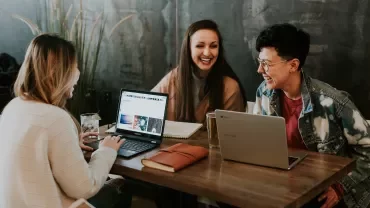 Gruppe mensen lacht en werkt samen met laptops aan tafel.