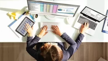 Individual at desk with computer, laptop, and tablet displaying data.