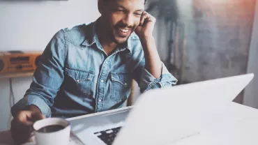 Person smiling while using a laptop and holding a coffee.