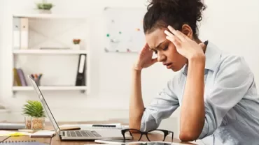 Een persoon werkt gefrustreerd aan een bureau met een laptop.