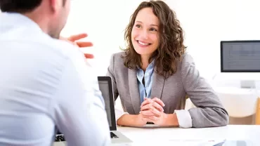 Two people having a business meeting at a desk with laptops.