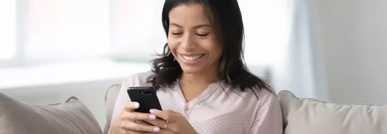 Person sitting on a couch, smiling while looking at a smartphone