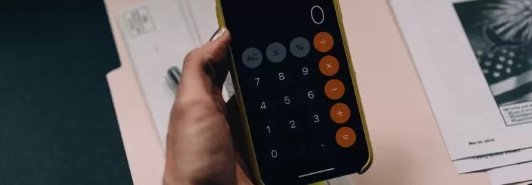 Telefoon met rekenmachine-app naast documenten op een bureau.