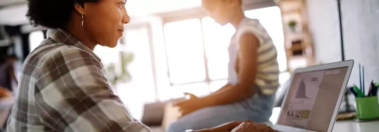 Person working on laptop with child in background.