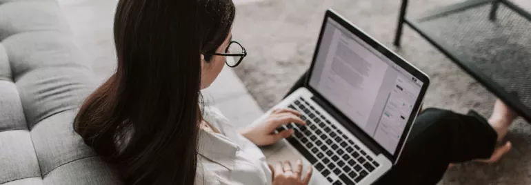 Persoon werkt op een laptop zittend op een bank.