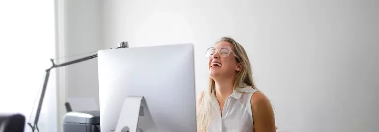 Persoon lacht achter groot computerscherm op bureau.