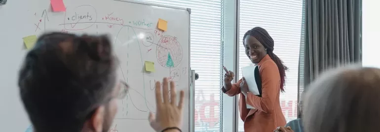 Presentatie van vrouw bij whiteboard met notities en grafieken.