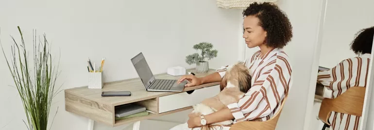 Person working at a desk with a laptop and a dog on their lap.