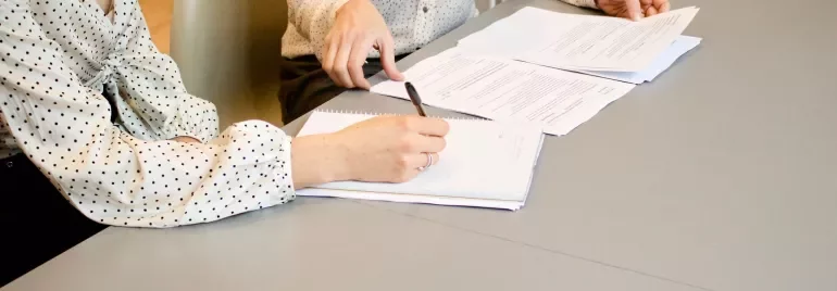 Twee mensen aan tafel met documenten en een notitieboek.