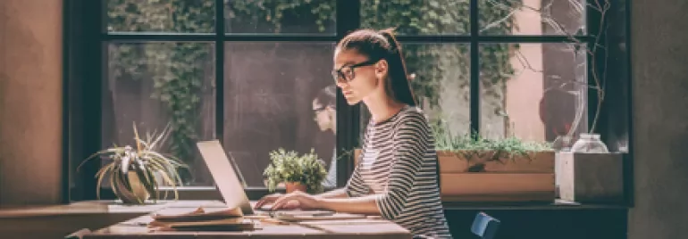 A person working on a laptop in a sunlight-filled café.