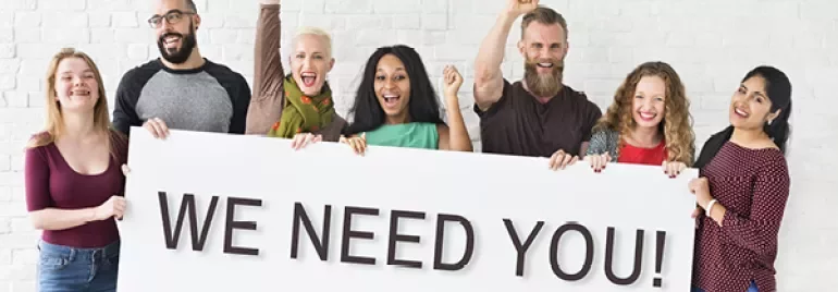 Group of people holding a sign that says 'WE NEED YOU!'