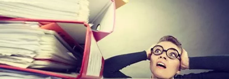 Person wearing glasses looking at a large stack of papers.