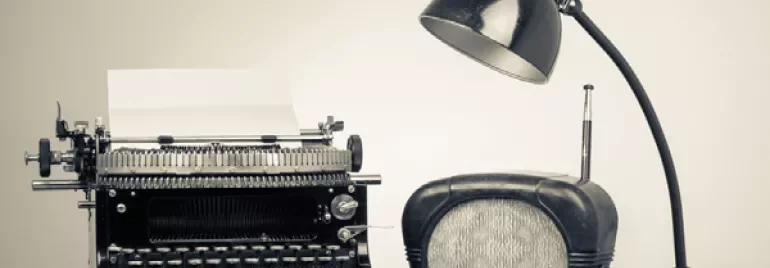 Typemachine met een retro radio en bureaulamp op een houten tafel.