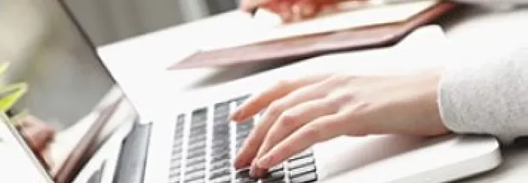 Een persoon typt op een laptop en maakt aantekeningen.