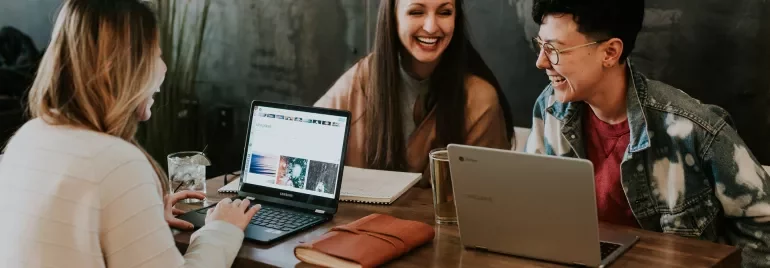Gruppe mensen lacht en werkt samen met laptops aan tafel.