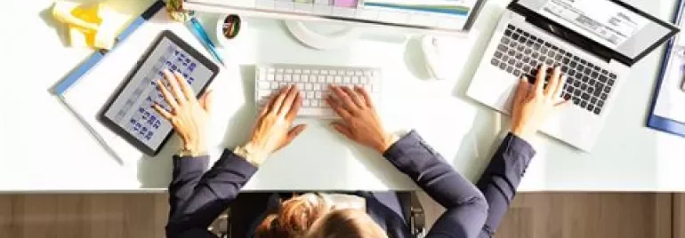 Persoon aan bureau met computer, laptop en tablet met gegevens.